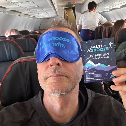 Man wearing sleep mask and holding ALTISNOOZE packet on a plane